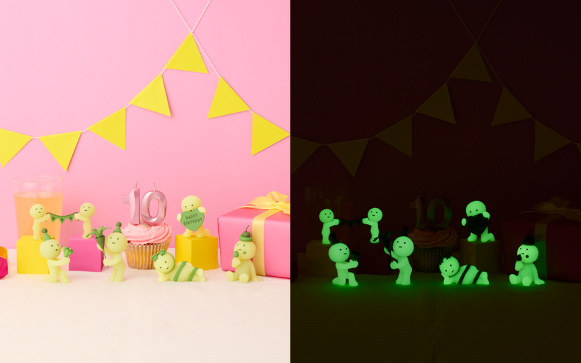 Glowing green figures on a dark background with a pink backdrop featuring yellow flags and birthday decorations.