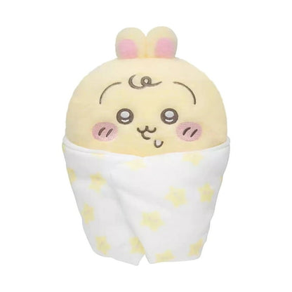 Plush toy resembling a cartoon character wrapped in a blanket with yellow polka dots on a white background