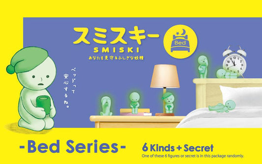 Dreams SMISKI Bed Series mini figures glowing in the dark on a nightstand, including poses of Smiski reading a book, crying, and sleeping next to a lamp and alarm clock.